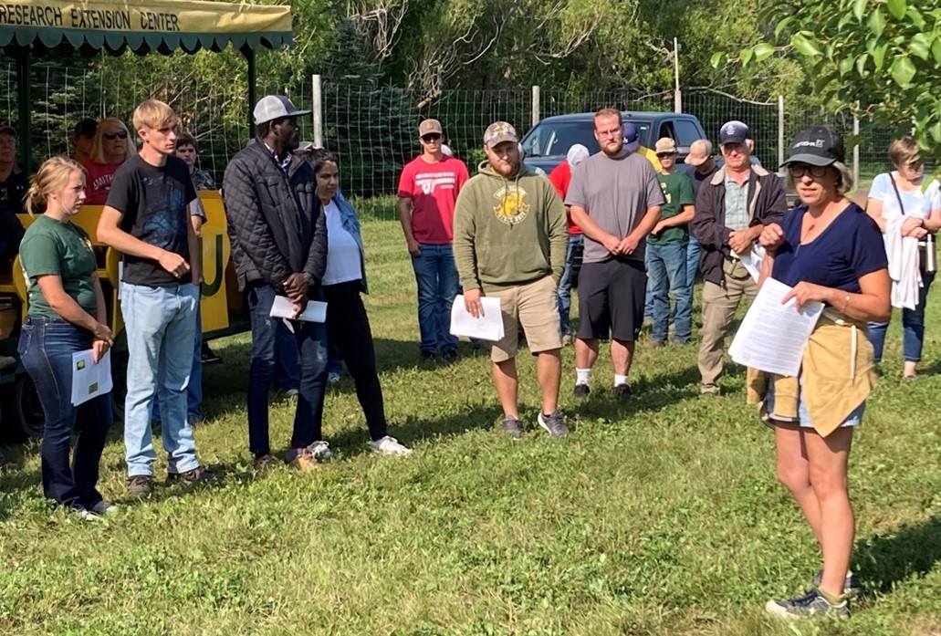 A group of people standing in the orchard as Gretchen Merryweather, on the right, speaks to them.