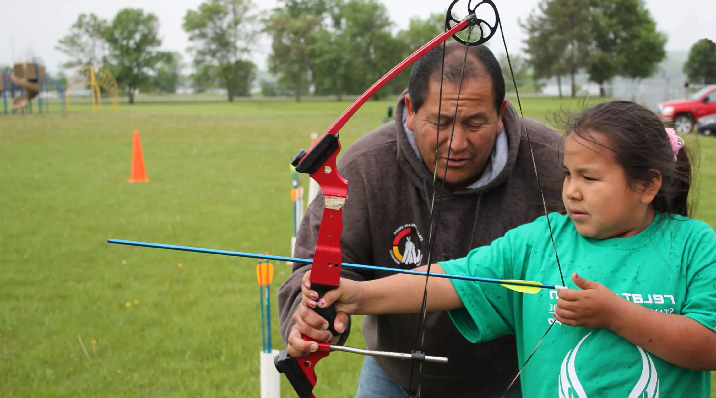 A 4-H volunteer helps a 4-H kid practice archery