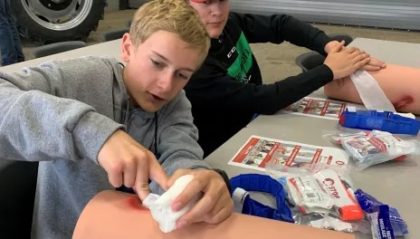 A young man practices stopping blood loss on a mannequin leg.