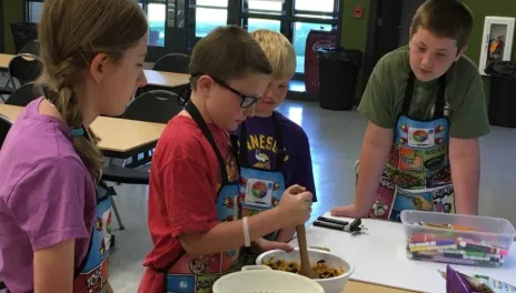 one child stirs cookie dough while 3 children observe