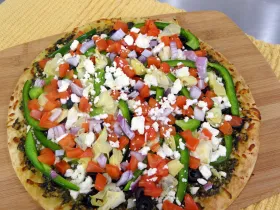 photograph of pesto pizza on a wooden cutting board