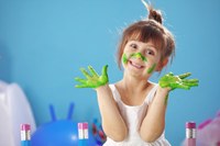 Smiley Kindergartener with bright green paint covering their hands and nose and cheeks