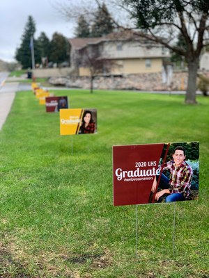 Rectangular signs with images of graduating seniors are arranged in a row across green lawn