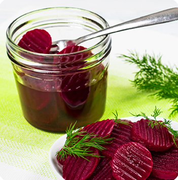 A jar of pickled beets sitting next to a plate filled with pickled beets and garnished with fresh dill