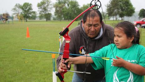 A 4-H volunteer helps a 4-H kid practice archery