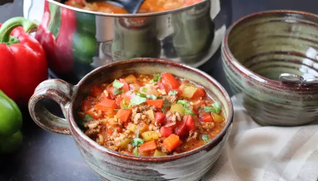 Stuffed Pepper Soup in a large cup on table next to red and green peppers