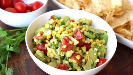 white bowl with tomatoes, corn and avocado salad with chips