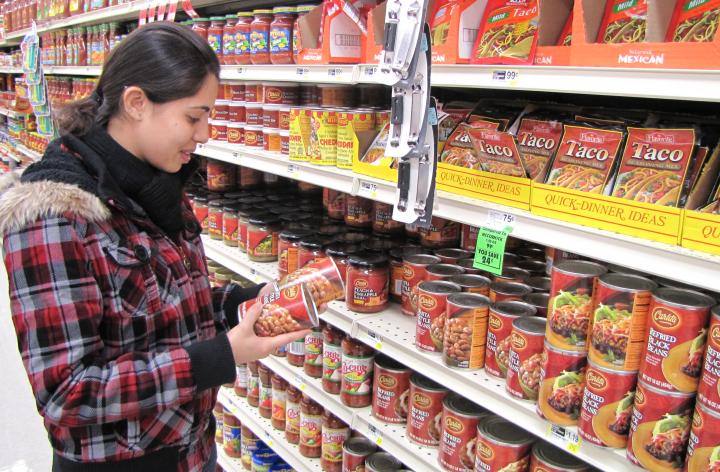 woman in grocery store aisle looking at canned food product