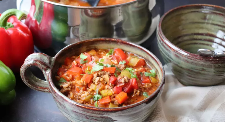 Stuffed Pepper Soup in a large cup on table next to red and green peppers