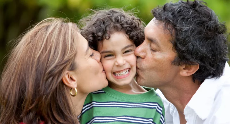 mother and father kissing son on each cheek