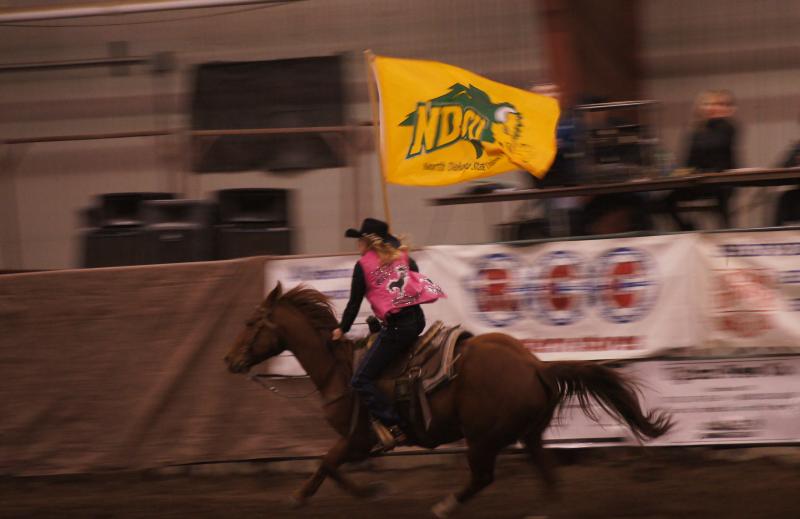 woman riding a horse in a rodeo with a NDSU flag