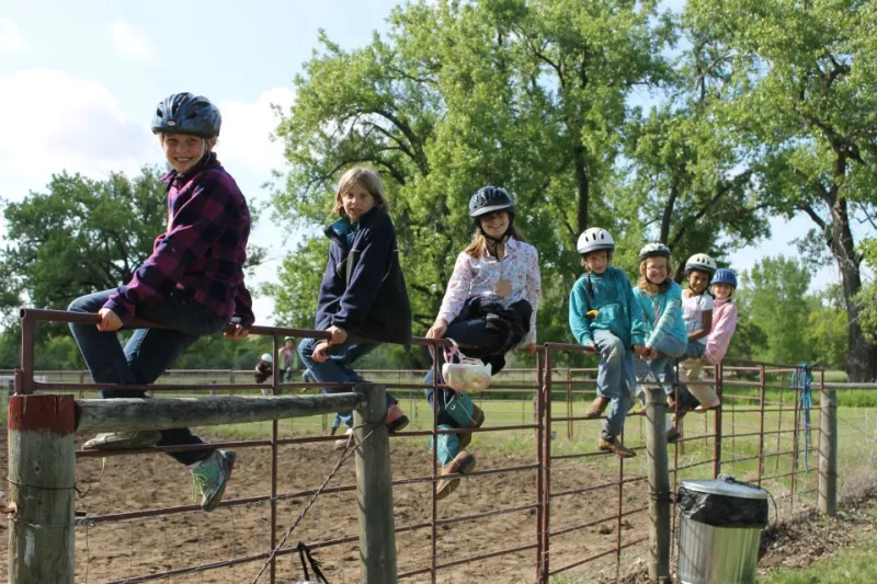 four girls sitting on top of horse fence