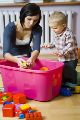 mother showing young toddler how to play with a toy